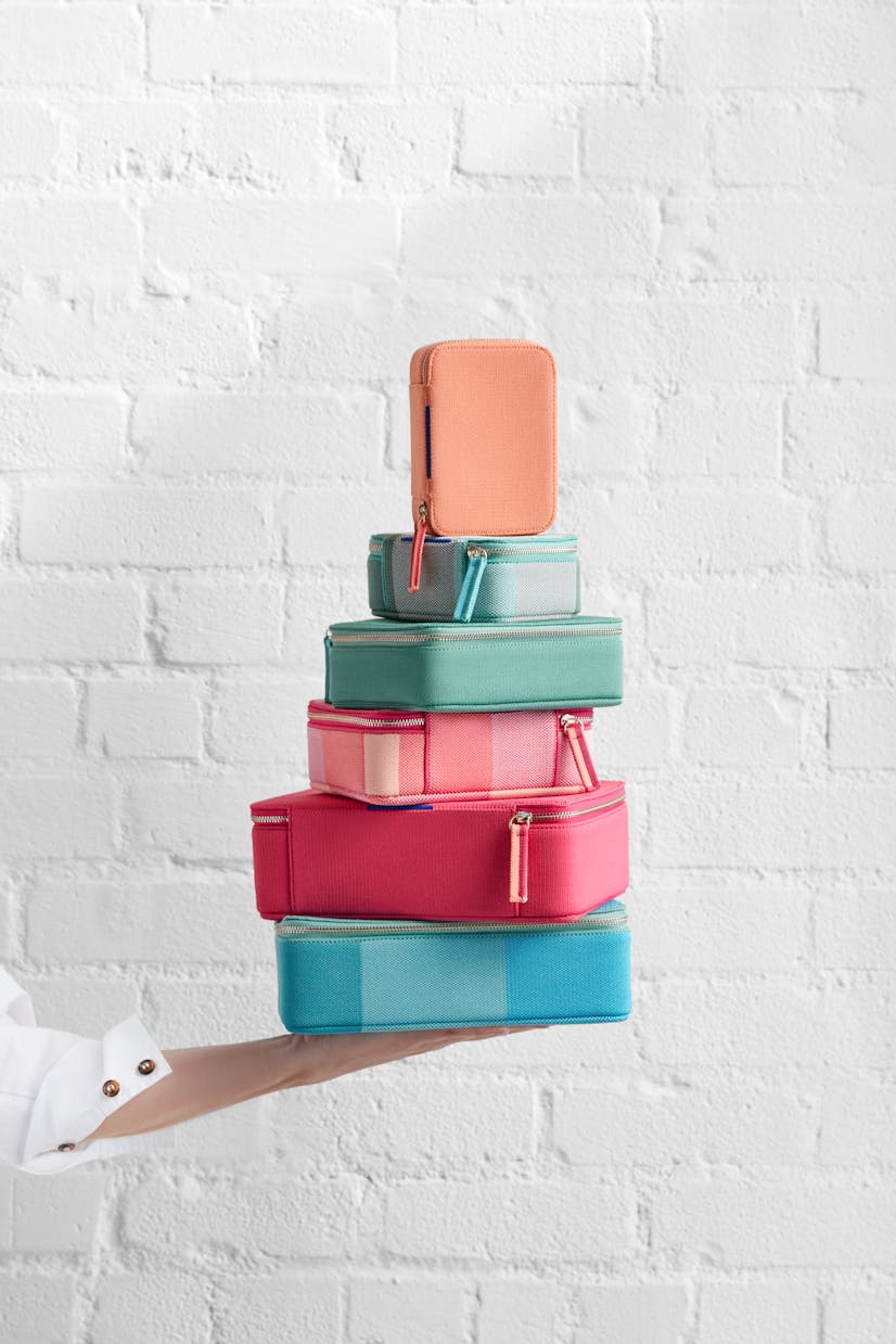 The Mini Catchall in Light Melon, The Mini Catchall in Juniper Madras, The Mid Catchall in Juniper Green, The Mid Catchall in Peach Madras, The Large Catchall in Bright Fuchsia and The Large Catchall in Caribbean Madras shown stacked.