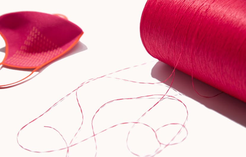 The Mask 1.0 in Pink shown next to a spool of Rothy’s signature thread.