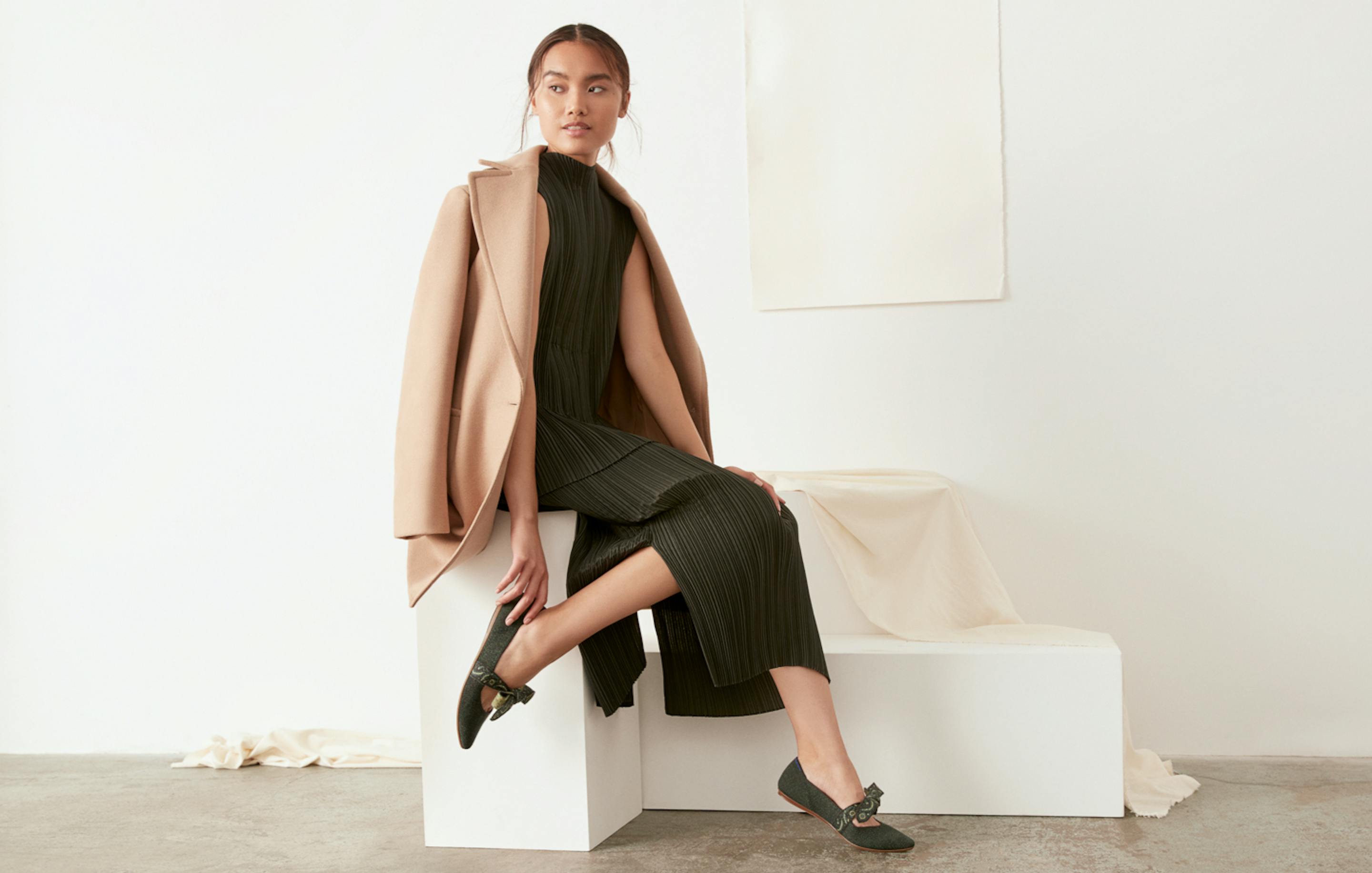 Model shown sitting on a white rectangular block, wearing The Merino Mary Jane in Forest Herringbone.