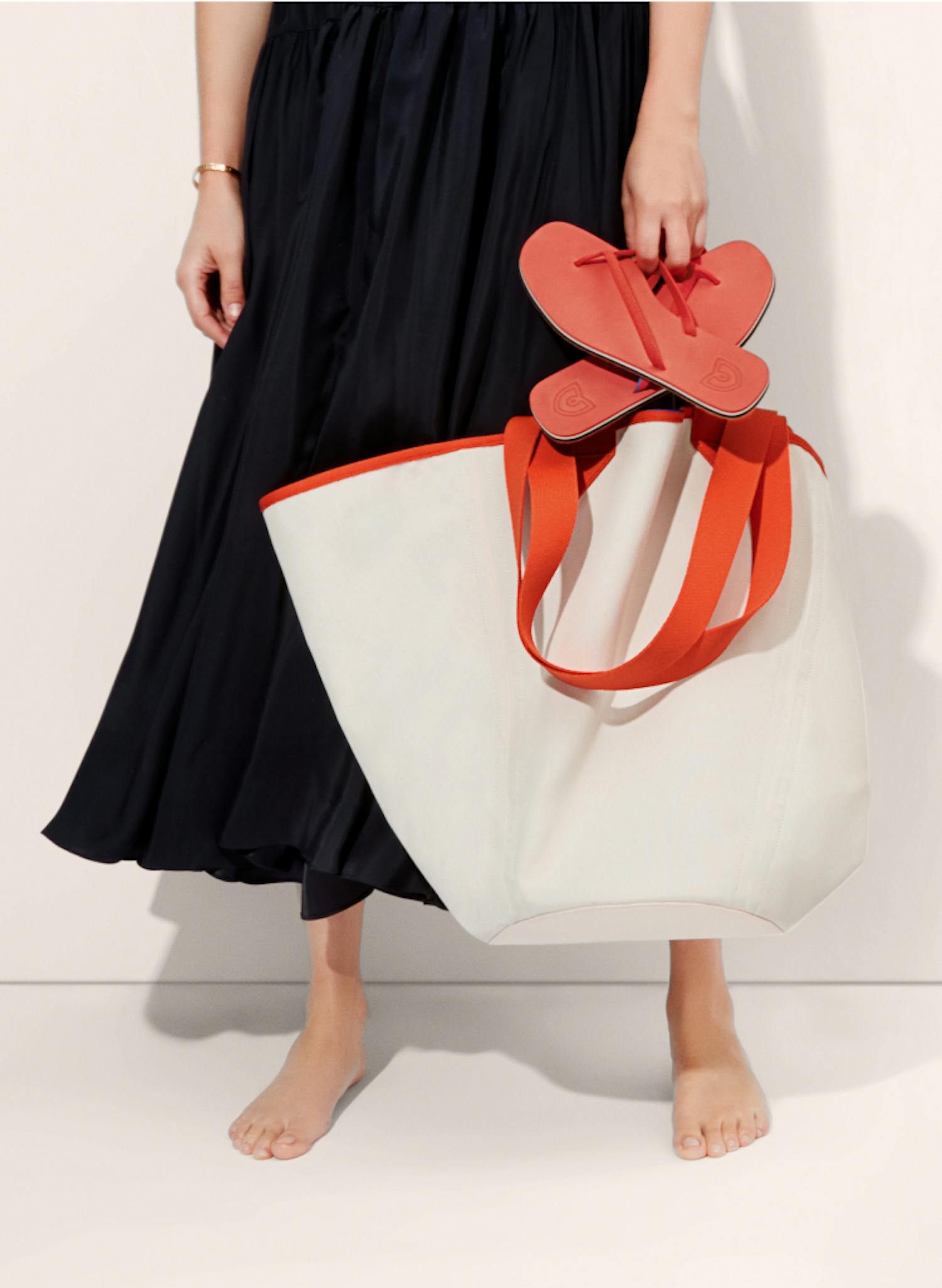 Model shot of a woman holding a pair of The Flip sandals and The Reversible Tote.