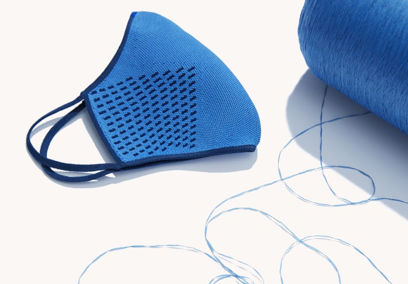 The Mask 1.0 in Blue folded next to a large spool of blue thread.