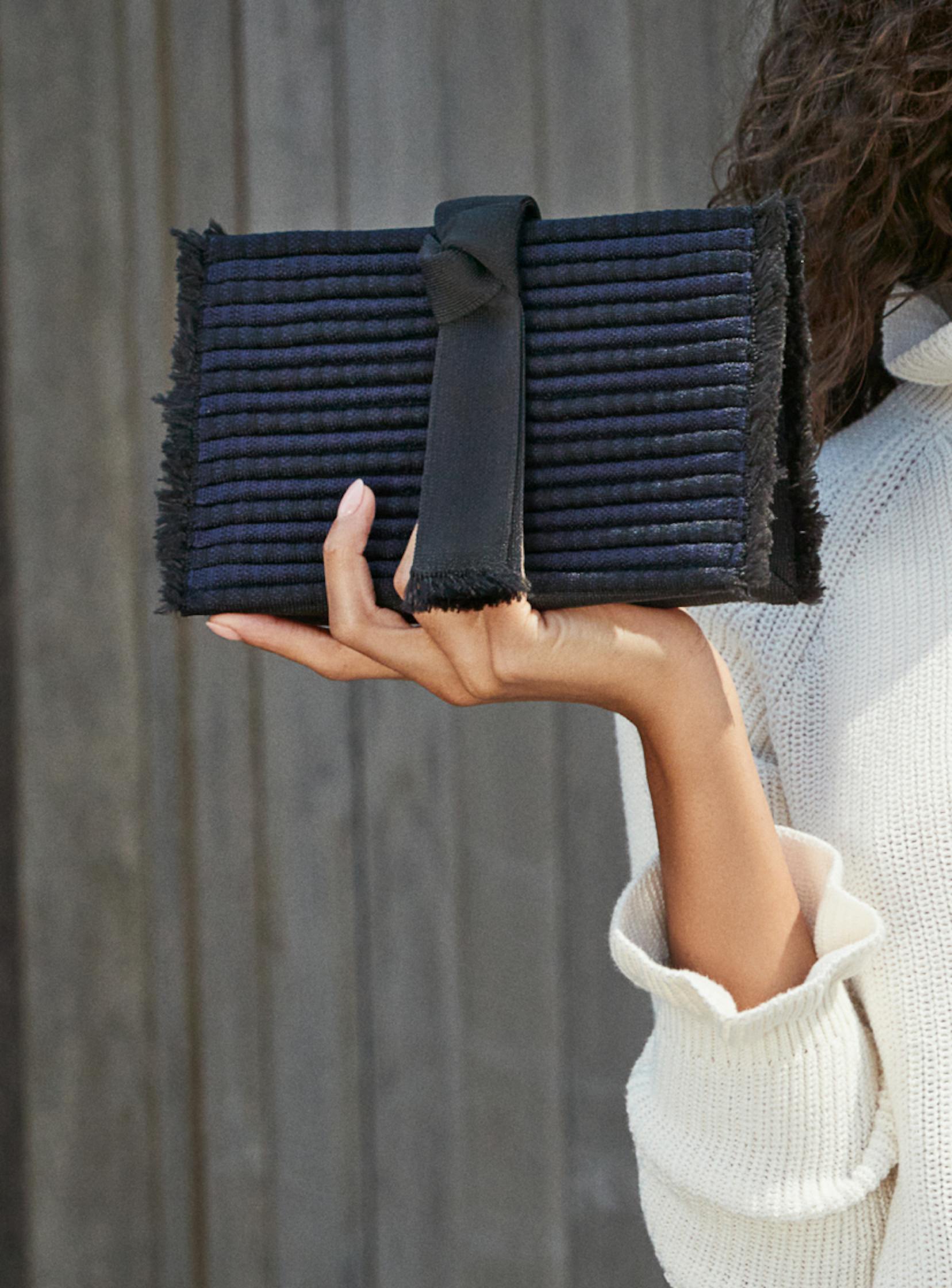 The Tassel Clutch in Onyx Blue held by a model.