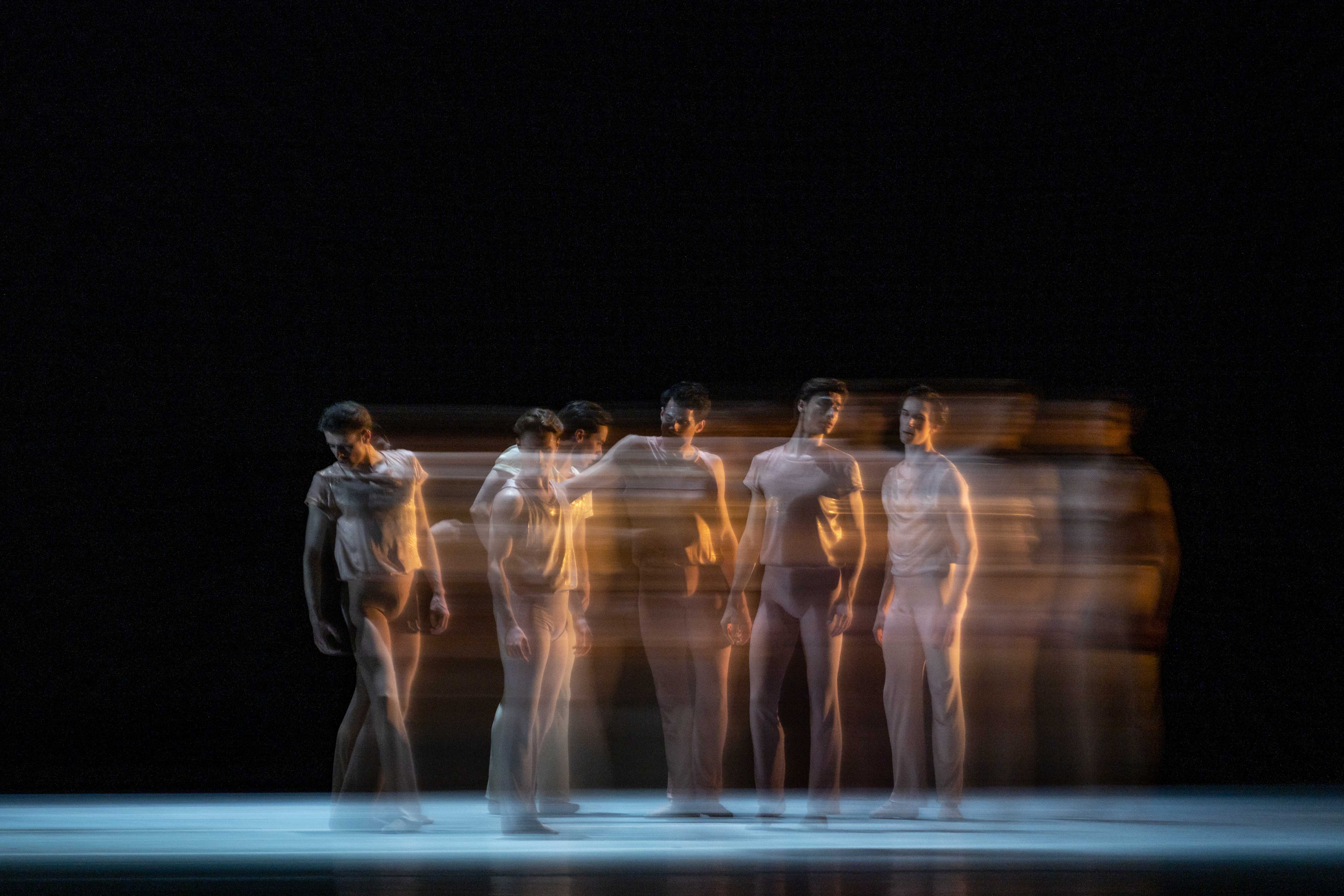 five dancers stand tall. The way the photograph has been taken makes them look like they are in motion as their bodies blur. 