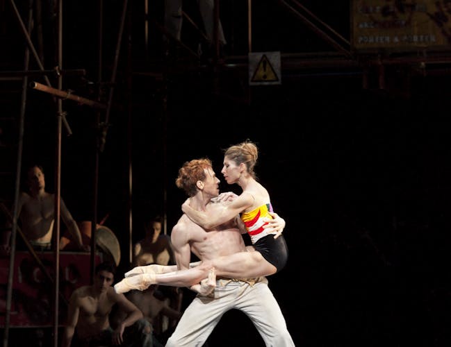 A topless man holds a woman in his arms