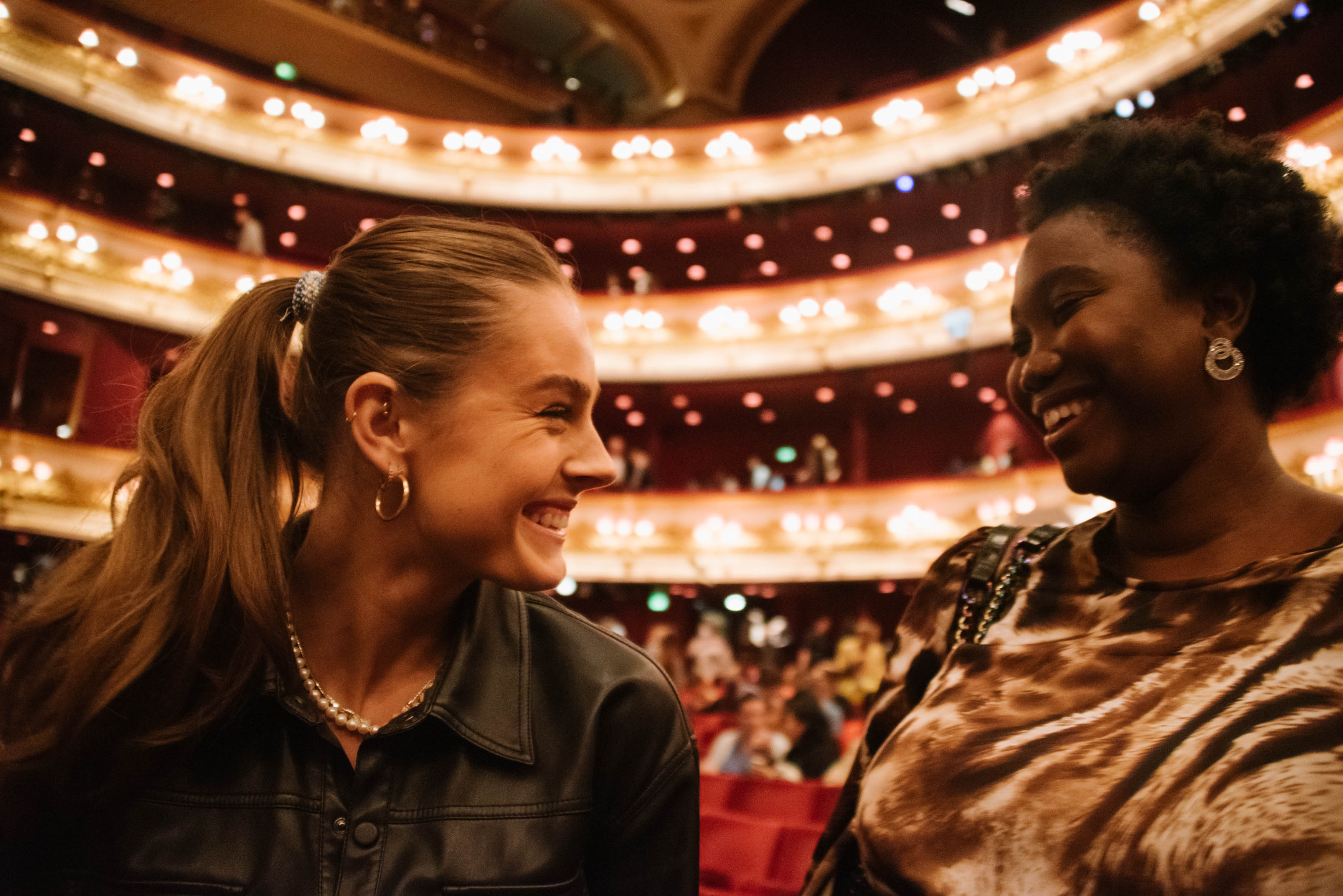 Two young women having a conversation in the main auditorium of the Royal Opera House.