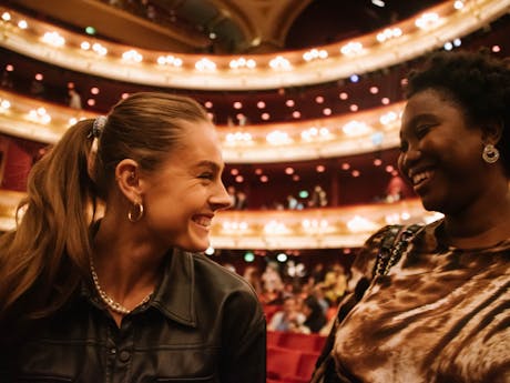 Two young women having a conversation in the main auditorium of the Royal Opera House.