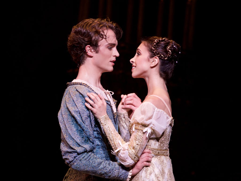 Two ballet dancers perform on stage: they are staring into each others eyes and embracing.