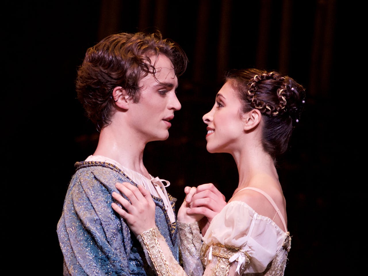 Two ballet dancers perform on stage: they are staring into each others eyes and embracing.