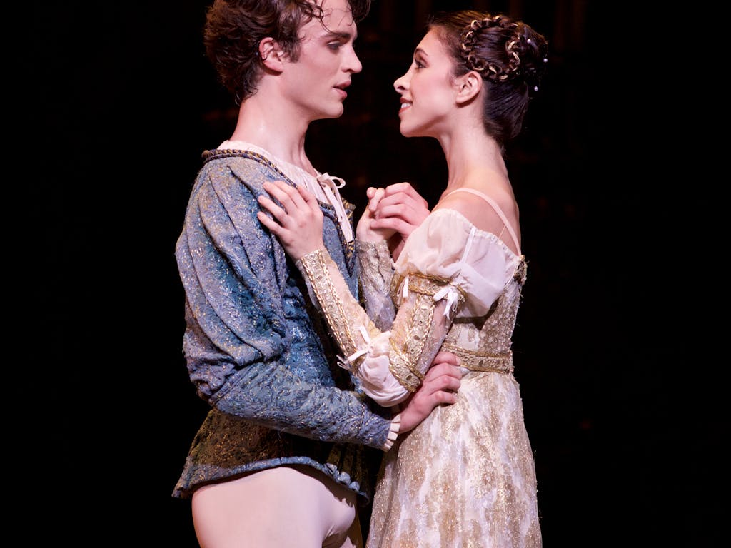 Two ballet dancers perform on stage: they are staring into each others eyes and embracing.