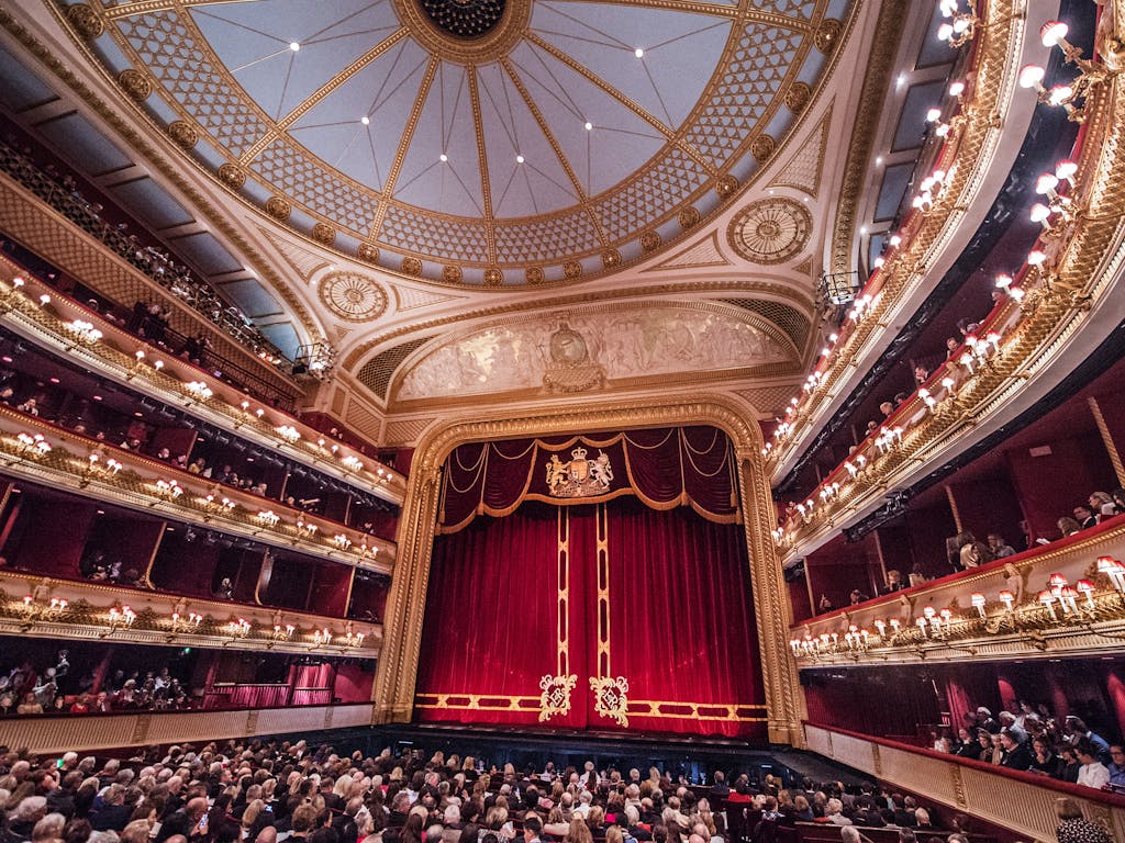 The main stage auditorium of the Royal Opera House. Taken from the Stalls of the auditorium, the house is full with patrons waiting for that night's performance to begin. 