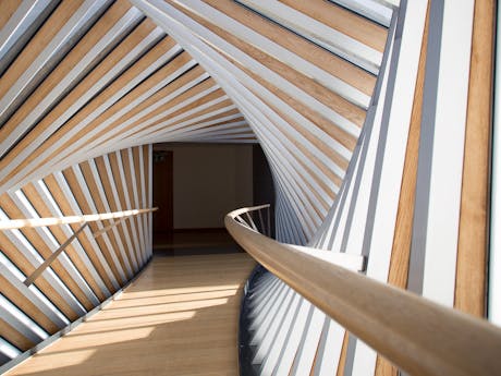 A pale wooden bridge encased in a tunnel of swirling geometric wooden lines stretching in front of the camera. The Bridge of Aspiration links the Royal Opera House and the Royal Ballet School.