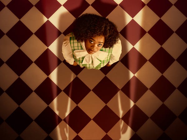 Opera singer Pretty Yende is photographed as Semele, a character from the opera of the same name. Semele is viewed from above, as she gazes at someone who casts a looming shadow over her.