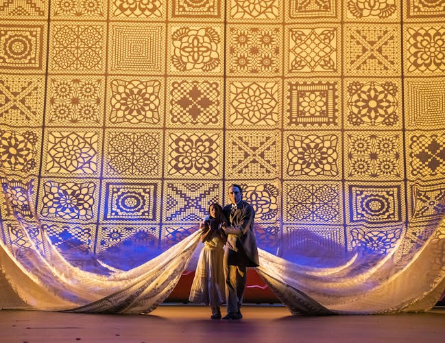 Two ballet dancers standing in front of a white backdrop during a performance.