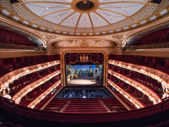 A view looking down at the seating, stage and circular ceiling the auditorium of the Royal Opera House