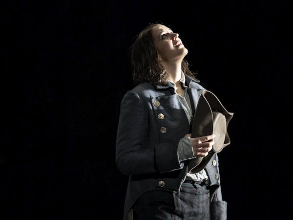 Female singer stands staring upwards. They are dressed in a guard's uniform.