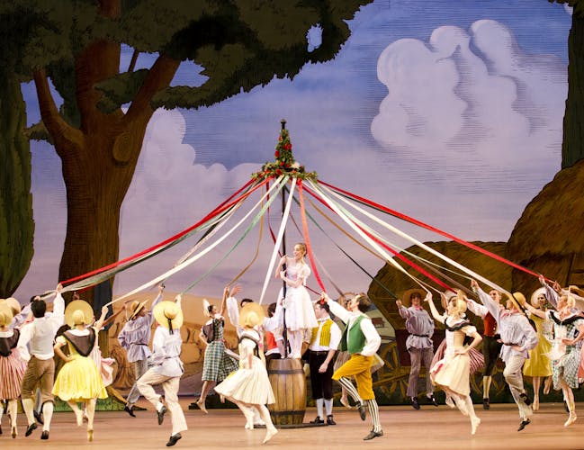 Several dancers skip in a circle holding onto the colourful ribbons of a maypole
