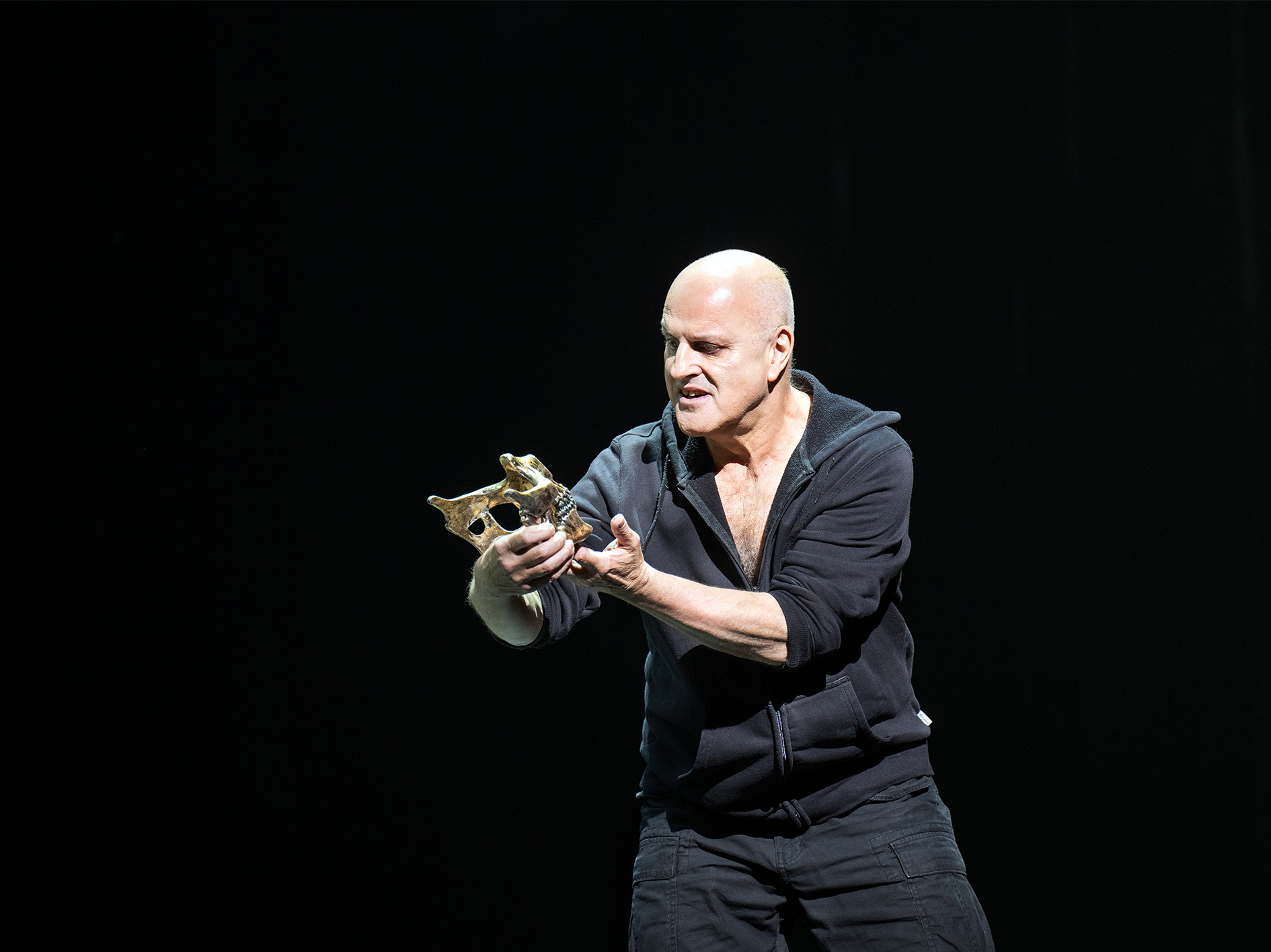 Actor Christopher Purves stands holding the lower portion of a skull in his hands and gazes upon it.