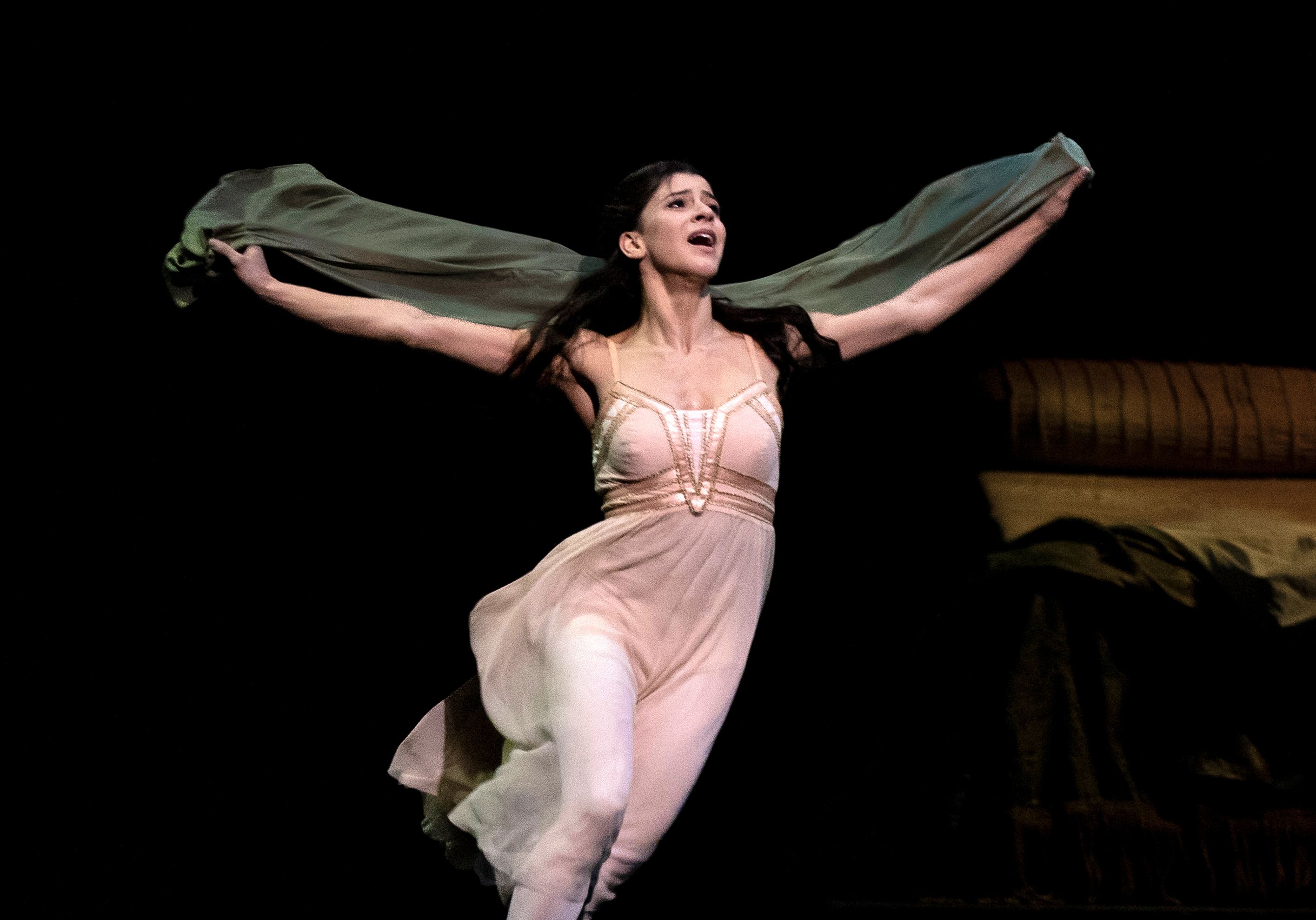 A ballet dancer in a pink dress with long black hair holds their arms upwards holding a shawl.