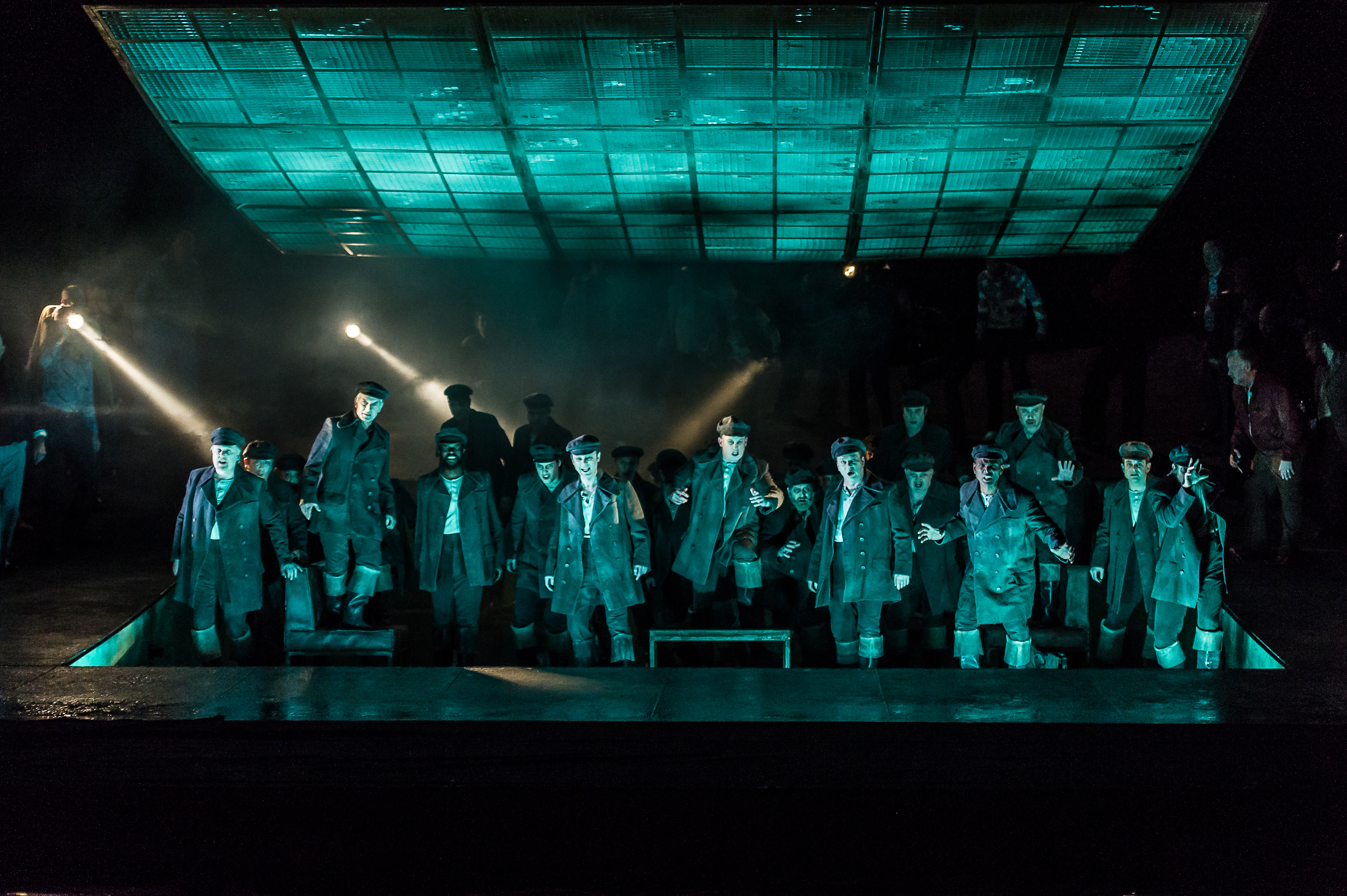 A group of sailors look out over the audience. They are bathed in green light as though light is reflecting off the water in front of them. 