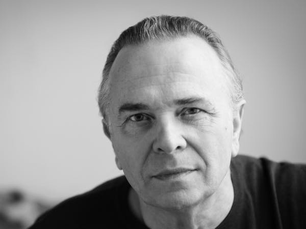 headshot of Sir Mark Elder in black and white. He's wearing a black tshirt and looking out at the camera.