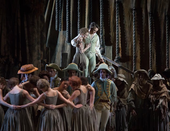 A group of Royal Ballet artists surround two dancers standing on a platform.