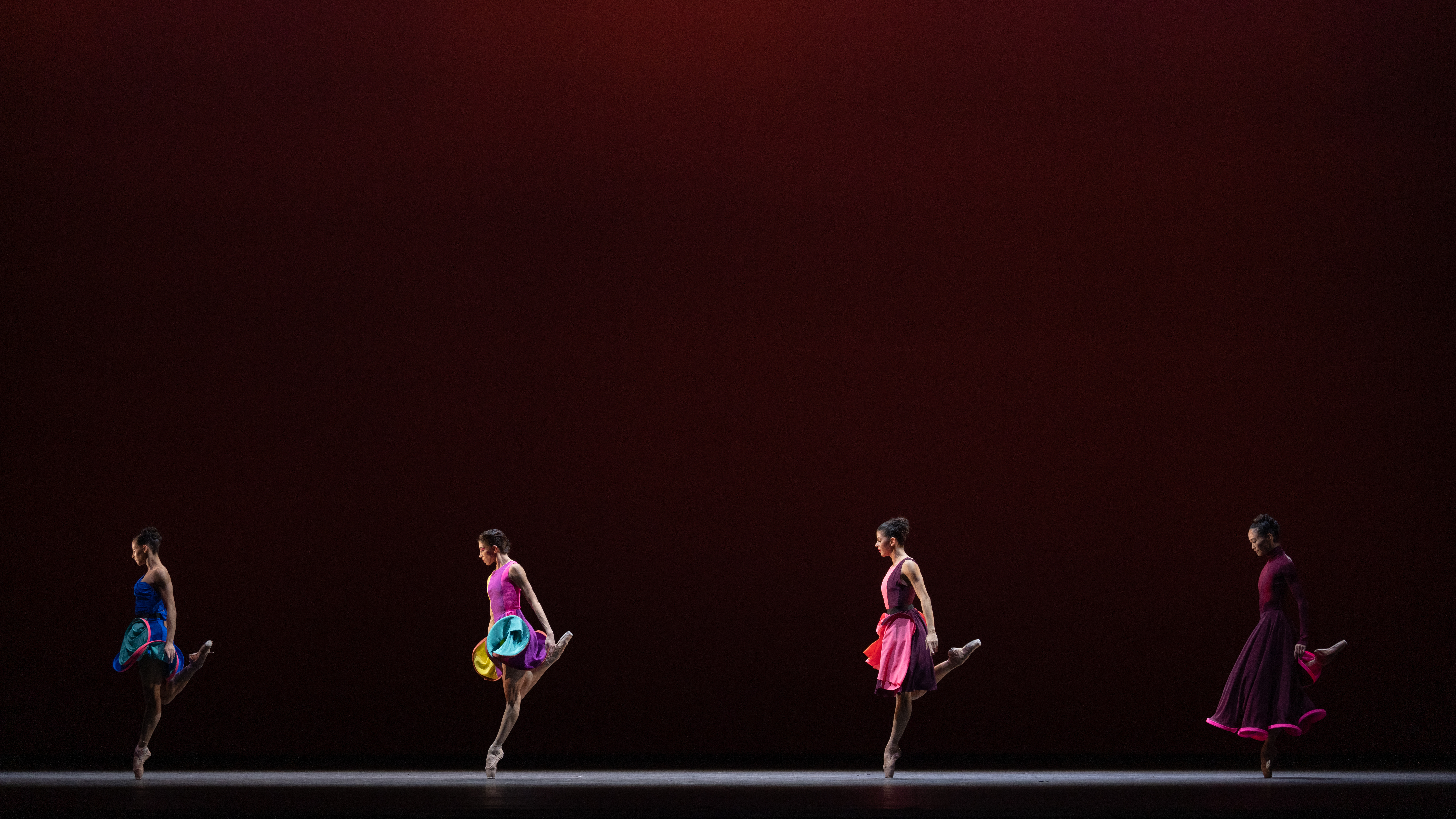 Four female dancers balance on one leg, standing in a line. They are wearing colourful dresses. (3 of 3)