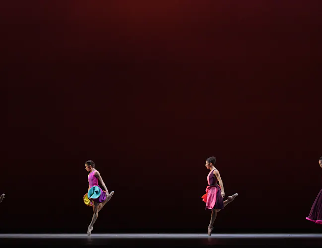 Four female dancers balance on one leg, standing in a line. They are wearing colourful dresses. (3 of 3)