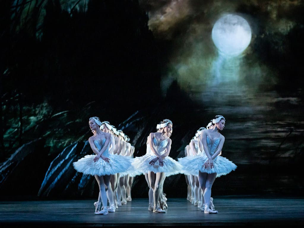 A group of Royal Ballet artists dance onstage in white tutus in a performance of Swan Lake.