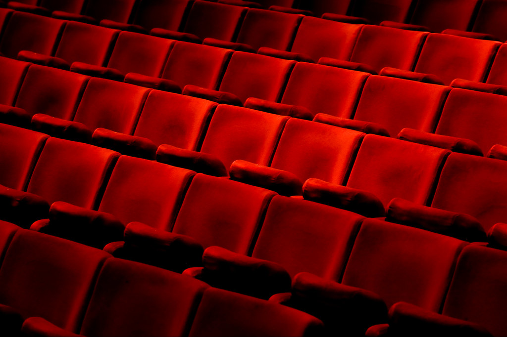 Five rows of vibrant red velvet theatre chairs with arm rests