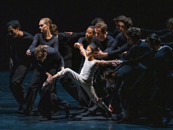 Several dancers wearing black hold onto a small child dressed in white, who appears to be running