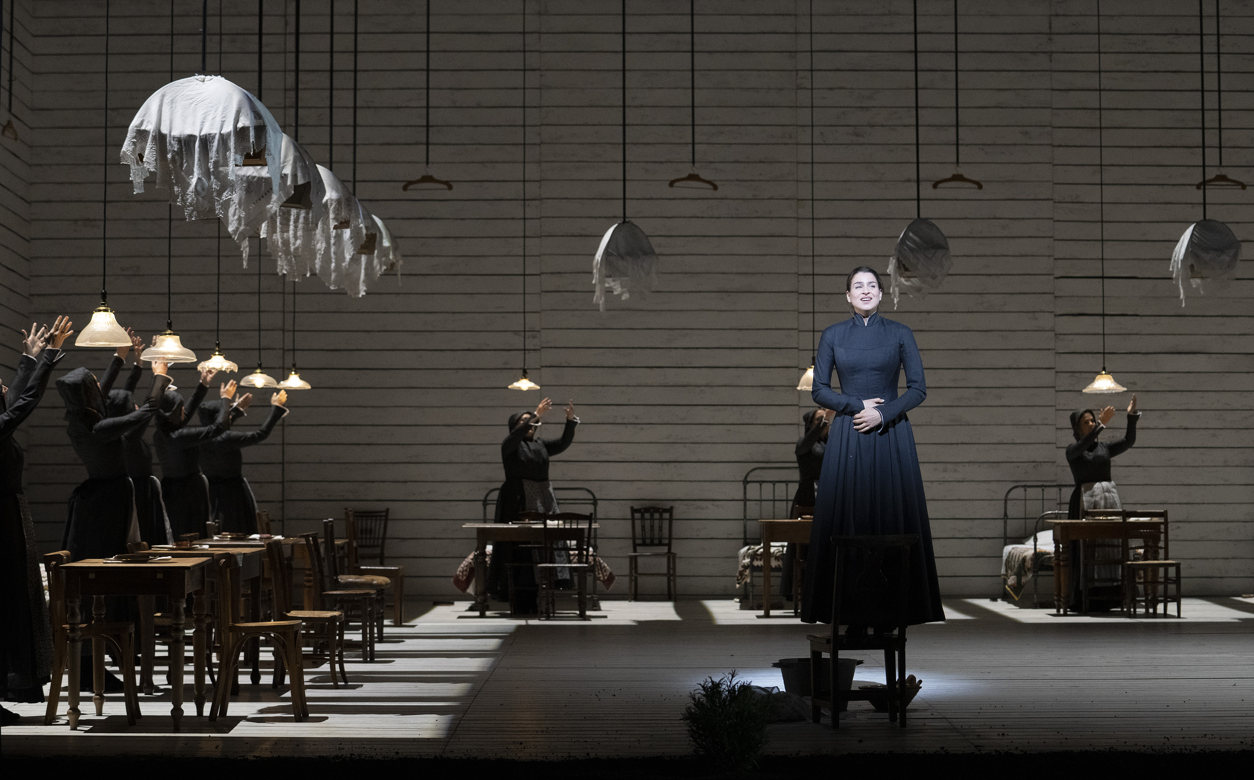 A woman in navy dress stands on a chair holding her hands over her stomach. 