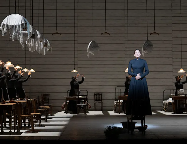 A woman in navy dress stands on a chair holding her hands over her stomach.