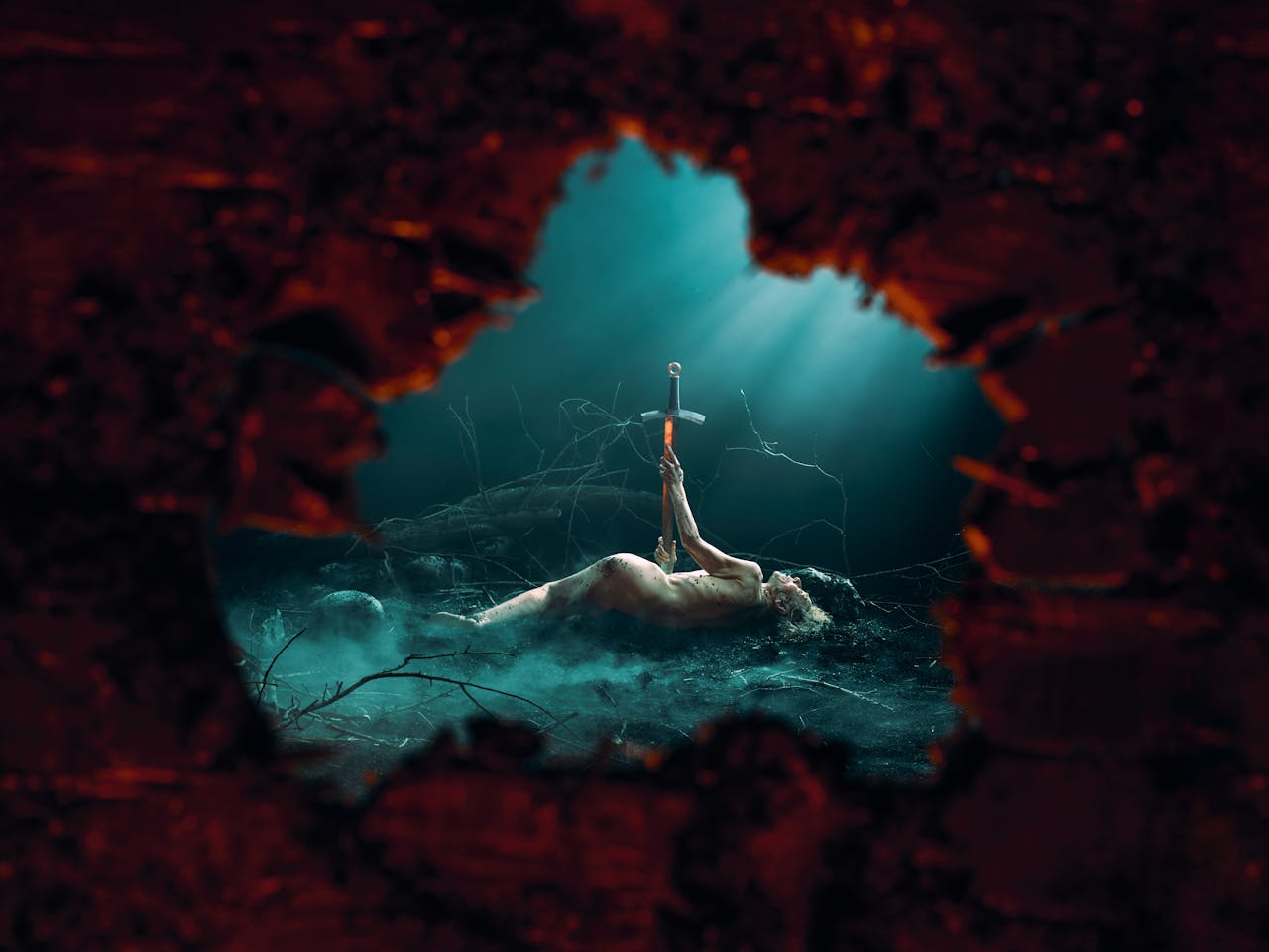 A naked man lies on a dark forest floor impaled by a large sword as the viewer watches from a hollowed tree.