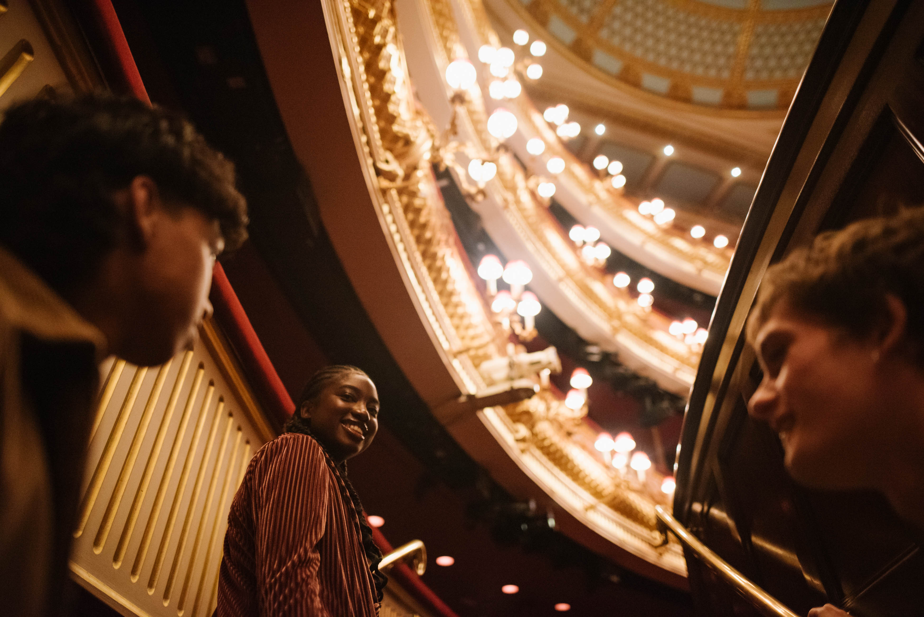 Three young people touring the main auditorium of the Royal Opera House.