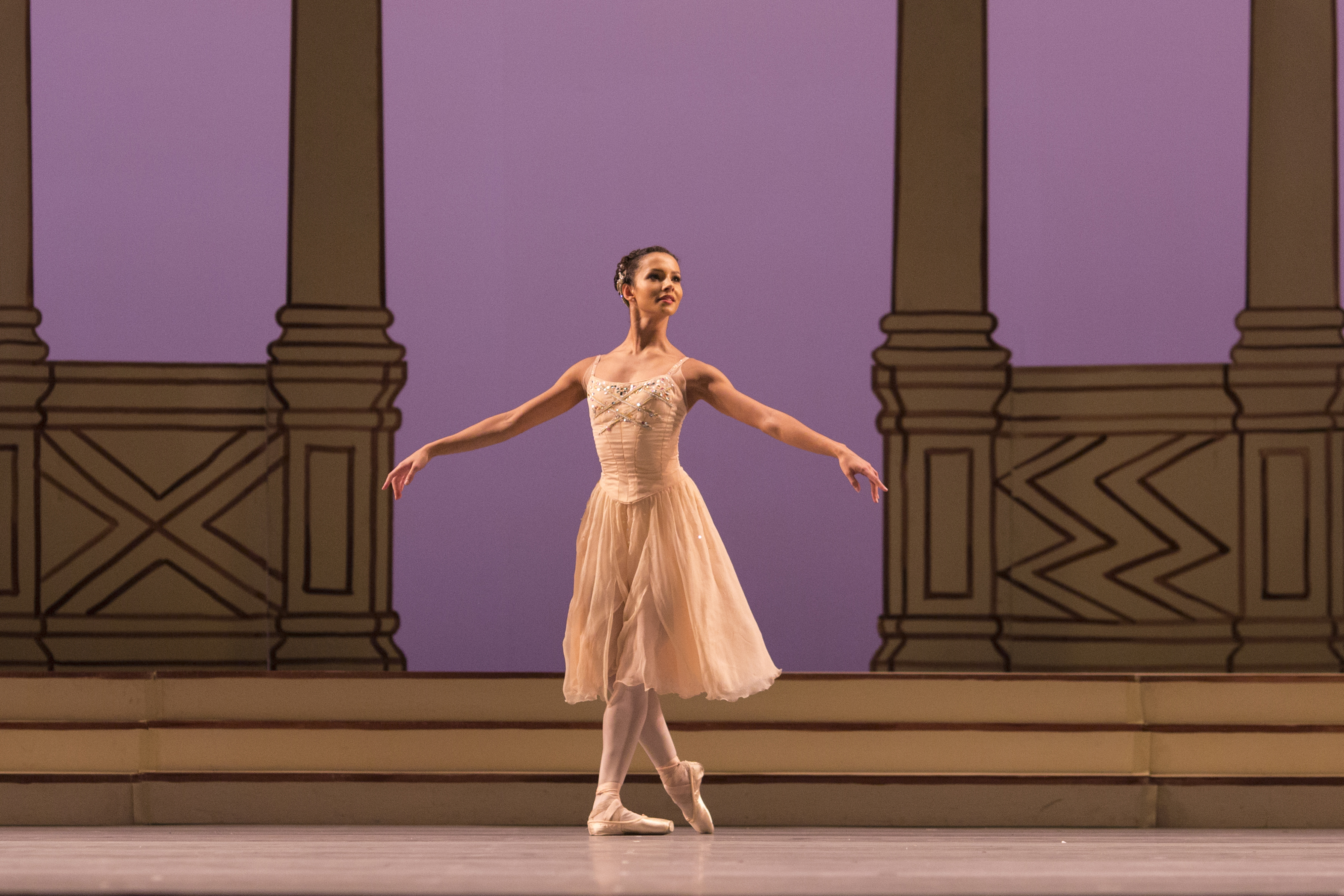 A dancer in a pink and white dress stands on stage between a series of columns. (7 of 8)