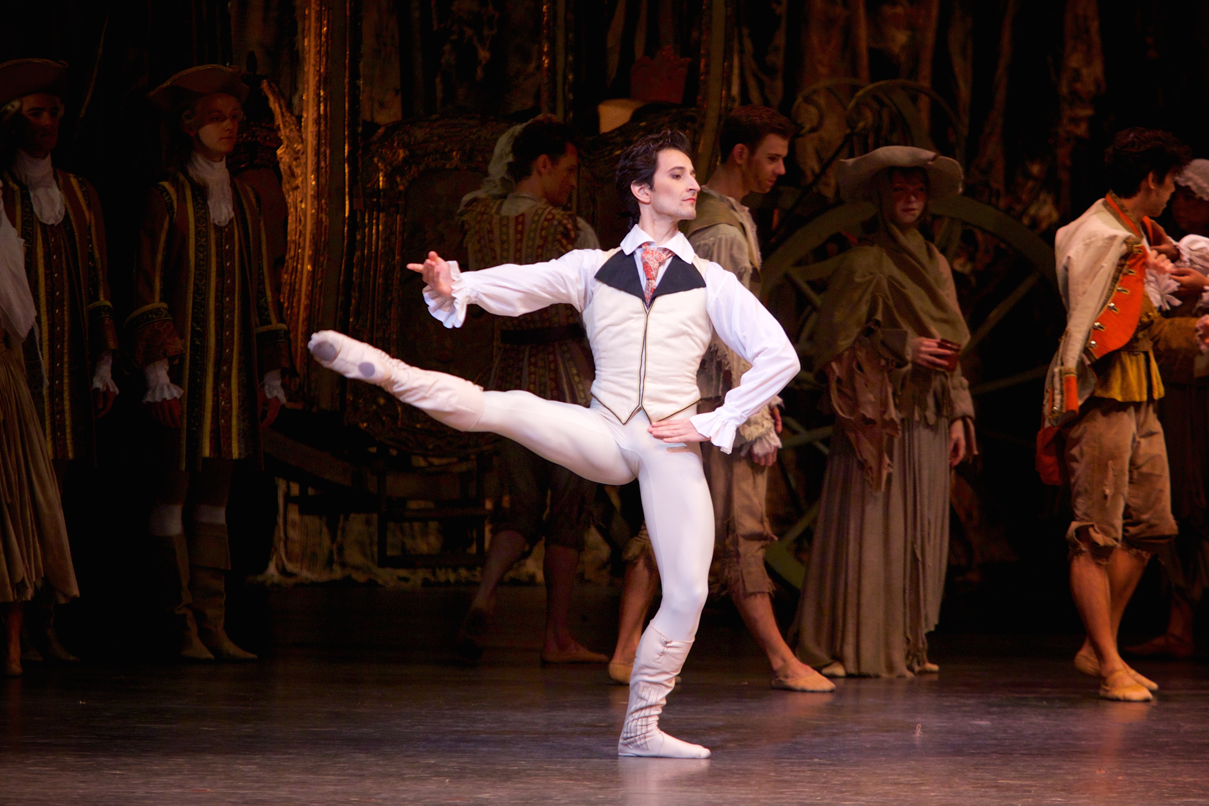 A dancer dressed as a Lord in a shirt and waistcoat balances on one leg in the centre of the stage