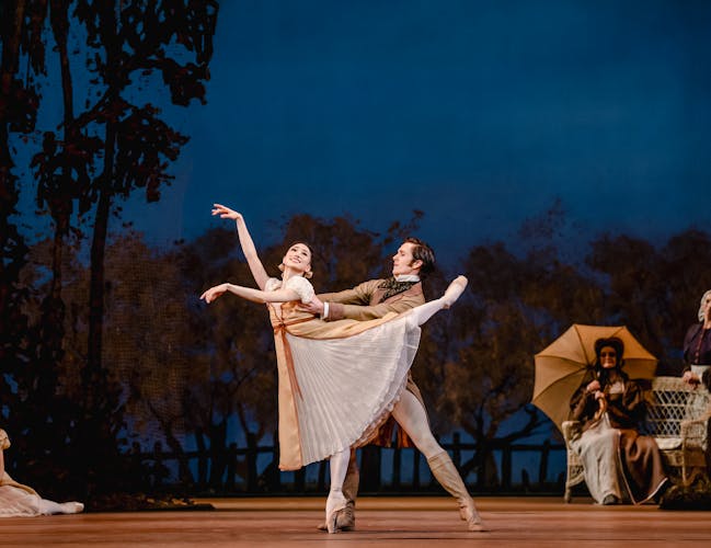 Akane Takada and William Bracewell as Olga and Lensky. They stand in a pose with her leg lifted high behind her as they gaze at each other.
