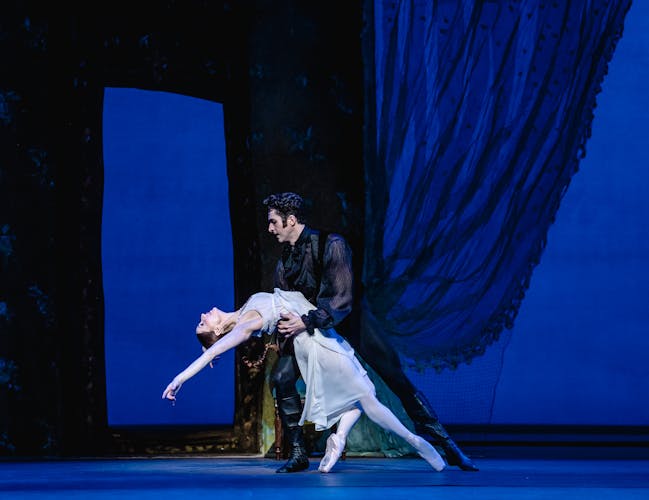 Marianela Nuñez and Reece Clarke as Tatiana Onegin. They are engaged in a passionate duet, with Onegin holding Tatiana's waist as she leans backward, her upper body arched gracefully.