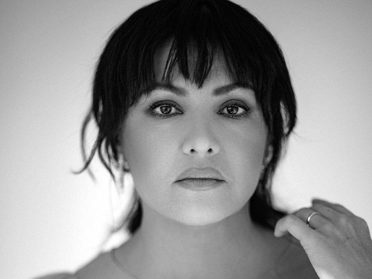 A black and white headshot of the opera singer Anna Netrebko. Her long dark hair is worn in a tony tail and she wears a light coloured pleated dress.