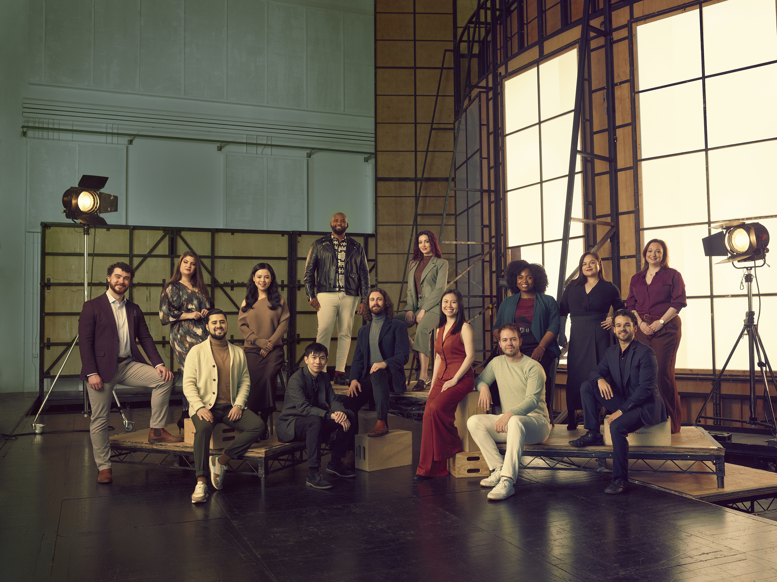 A group of people pose together in a studio setting, with lighting equipment and a large window backdrop.