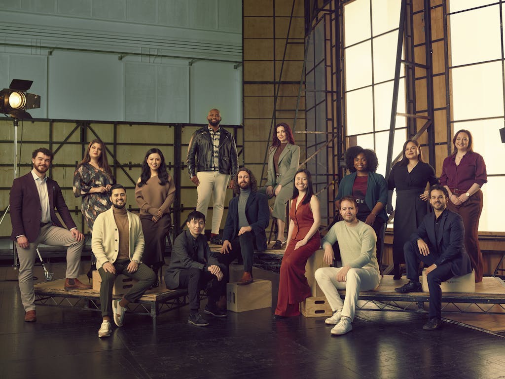 A group of people pose together in a studio setting, with lighting equipment and a large window backdrop.