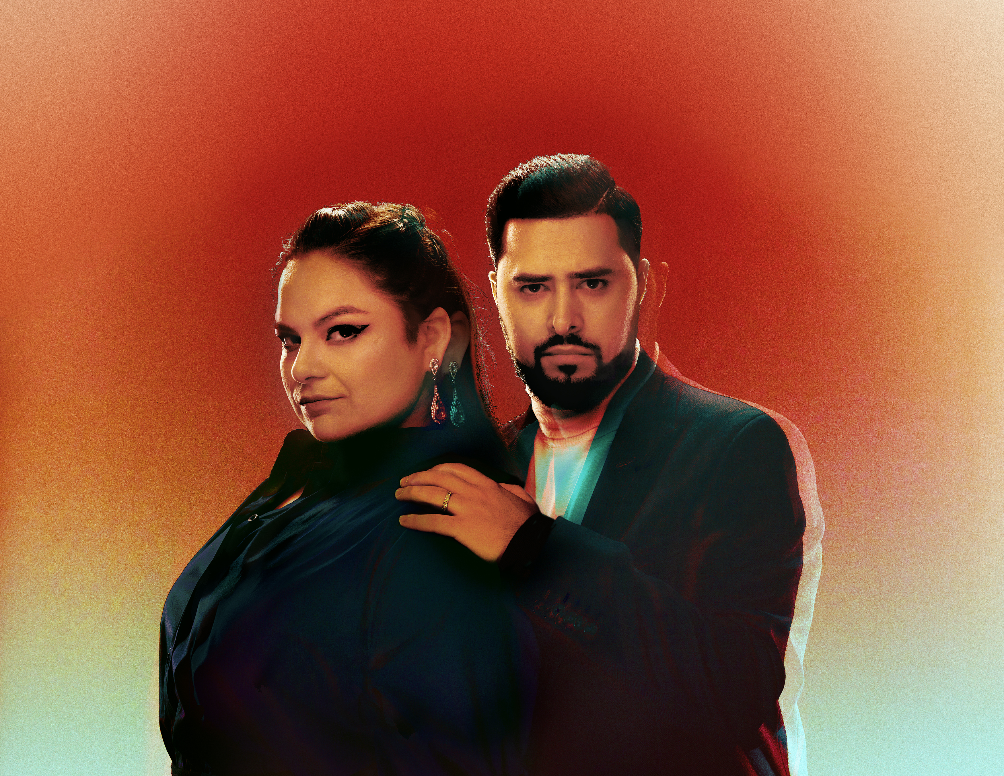 A person wearing all black stands sideways and another person who is also wearing all black holds their shoulder with their left hand facing the front. The background is set with gradient colours starting with orange moving down to blue-green.