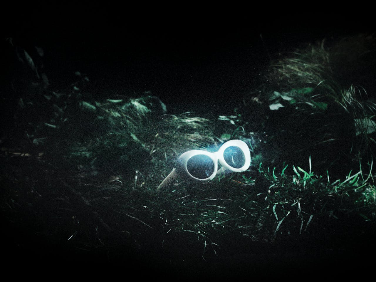 A pair of white 60s style framed sunglasses sit in amongst green grass. They represent the glasses worn by Kurt Cobain in The Royal Opera’s production of Last Days.