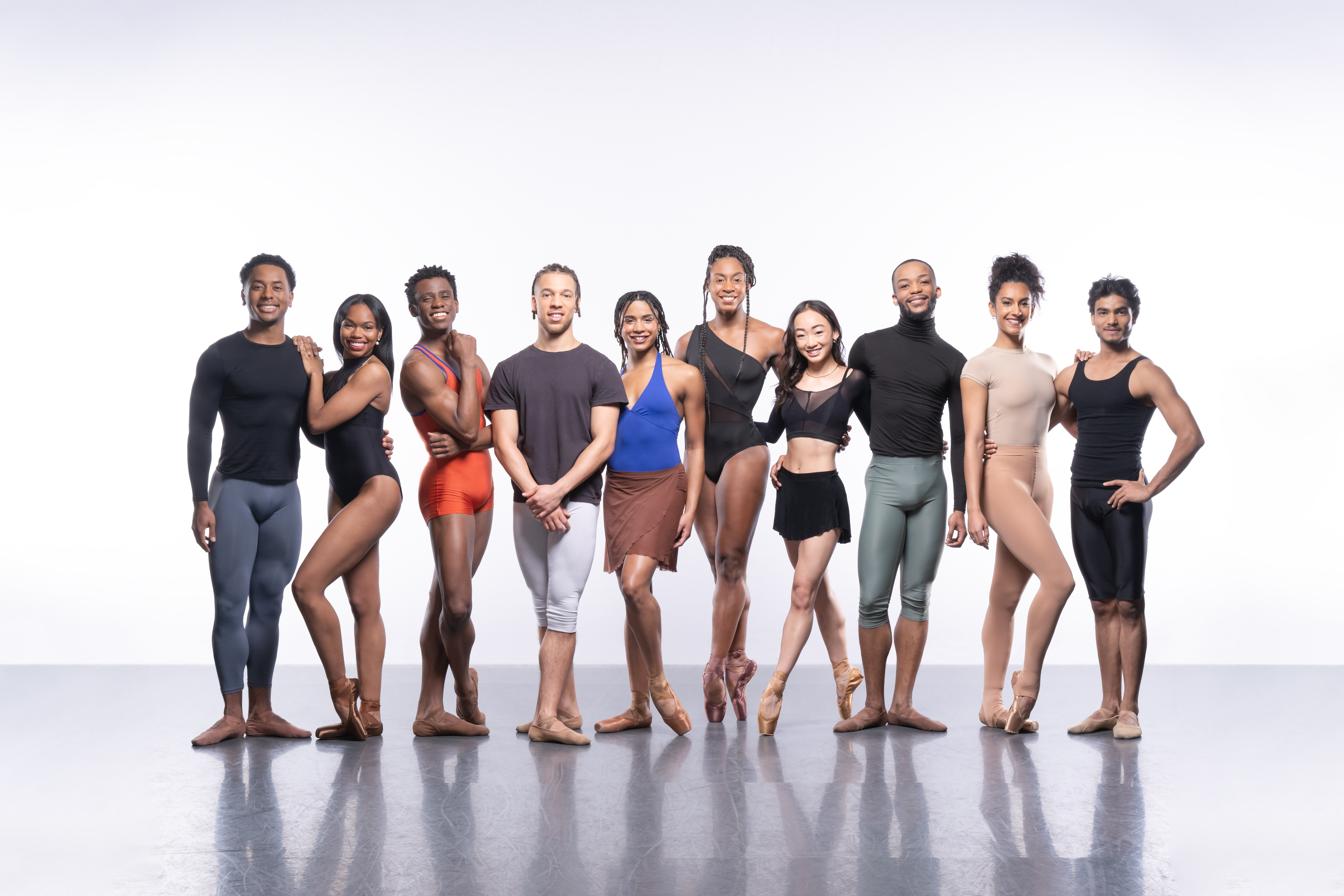 Ten ballet dancers stand in a bare studio, each wearing different types of rehearsal dance clothes. They are performers in The Royal Ballet’s Ballet Black.  