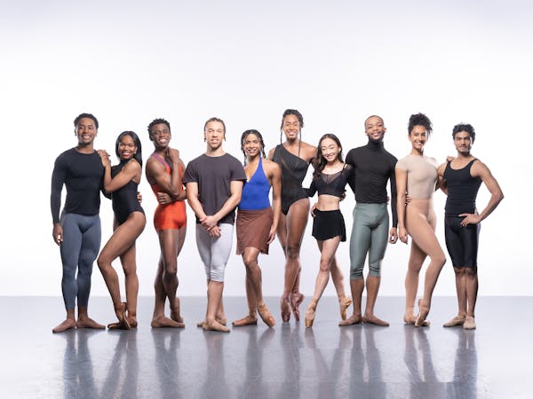 Ten ballet dancers stand in a bare studio, each wearing different types of rehearsal dance clothes. They are performers in The Royal Ballet’s Ballet Black.
