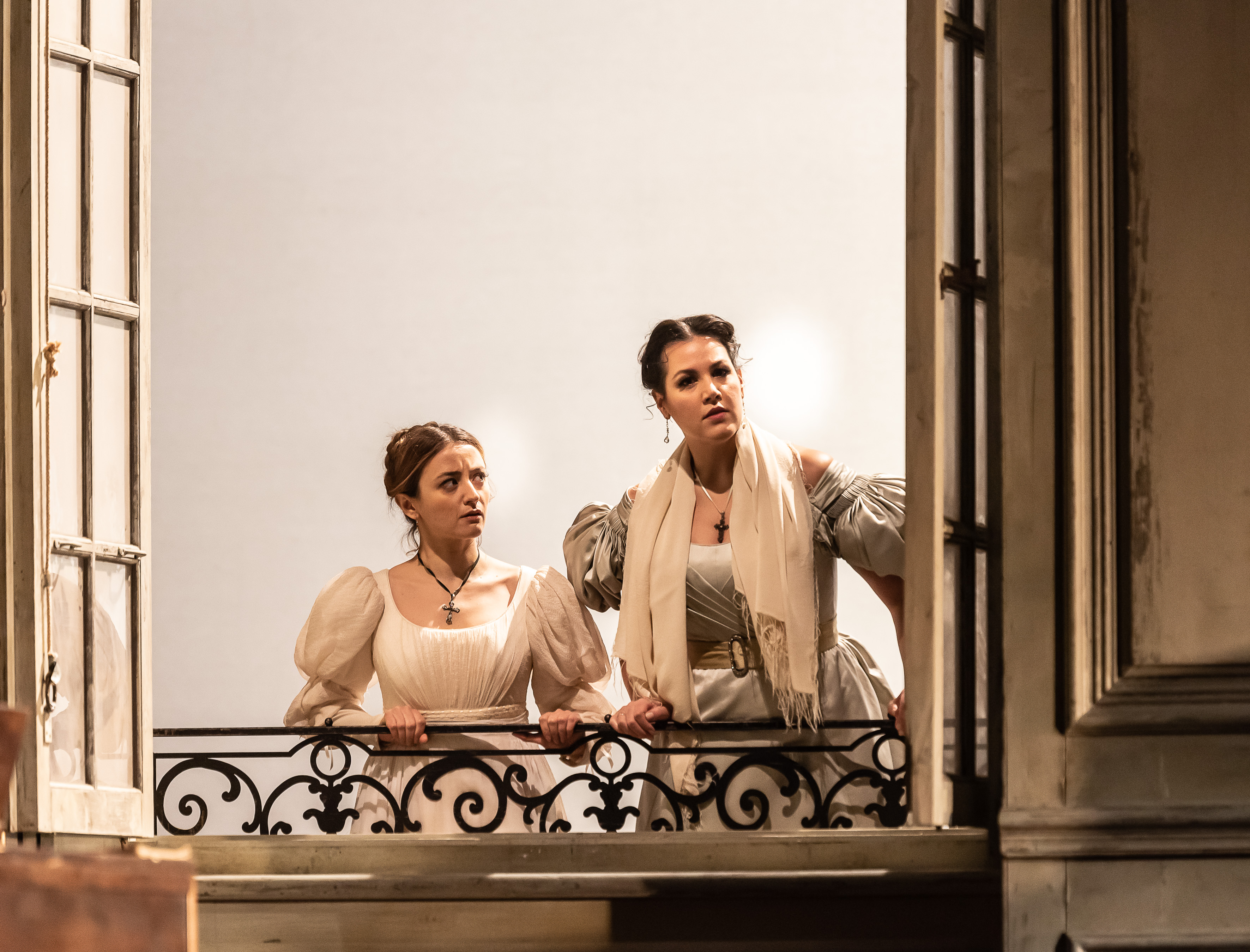 Two young women look out of a window. 