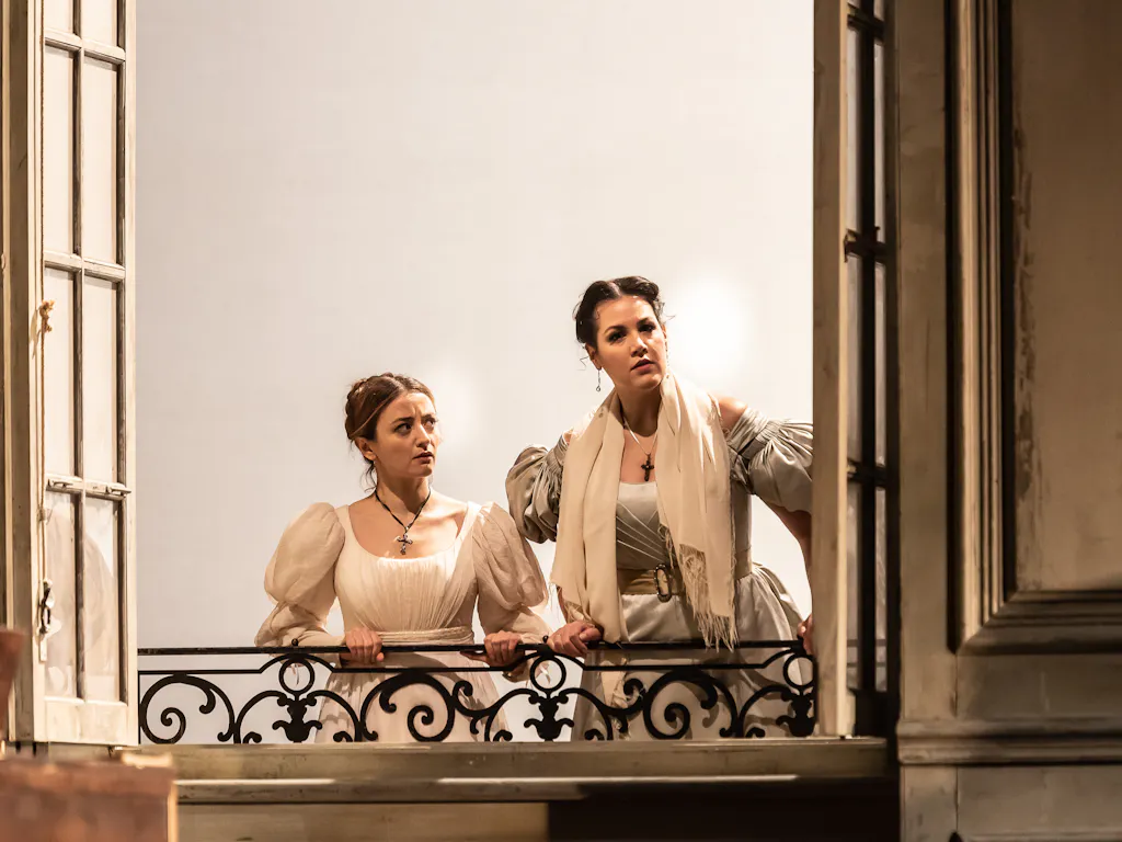 Two young women look out of a window.