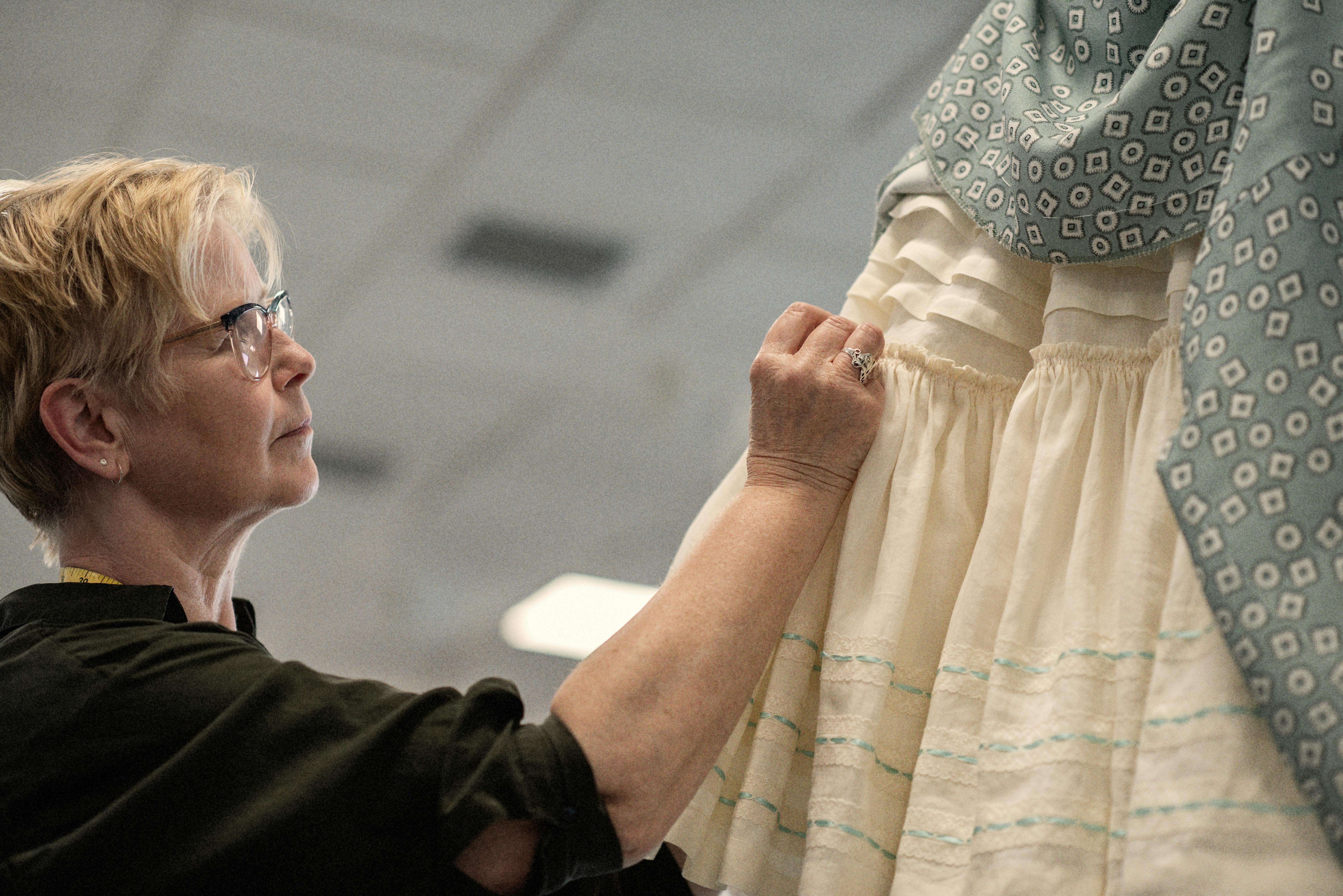 A woman makes adjustments to a blue and white ruffled dress in the Costume Production Workshop at the Royal Opera House