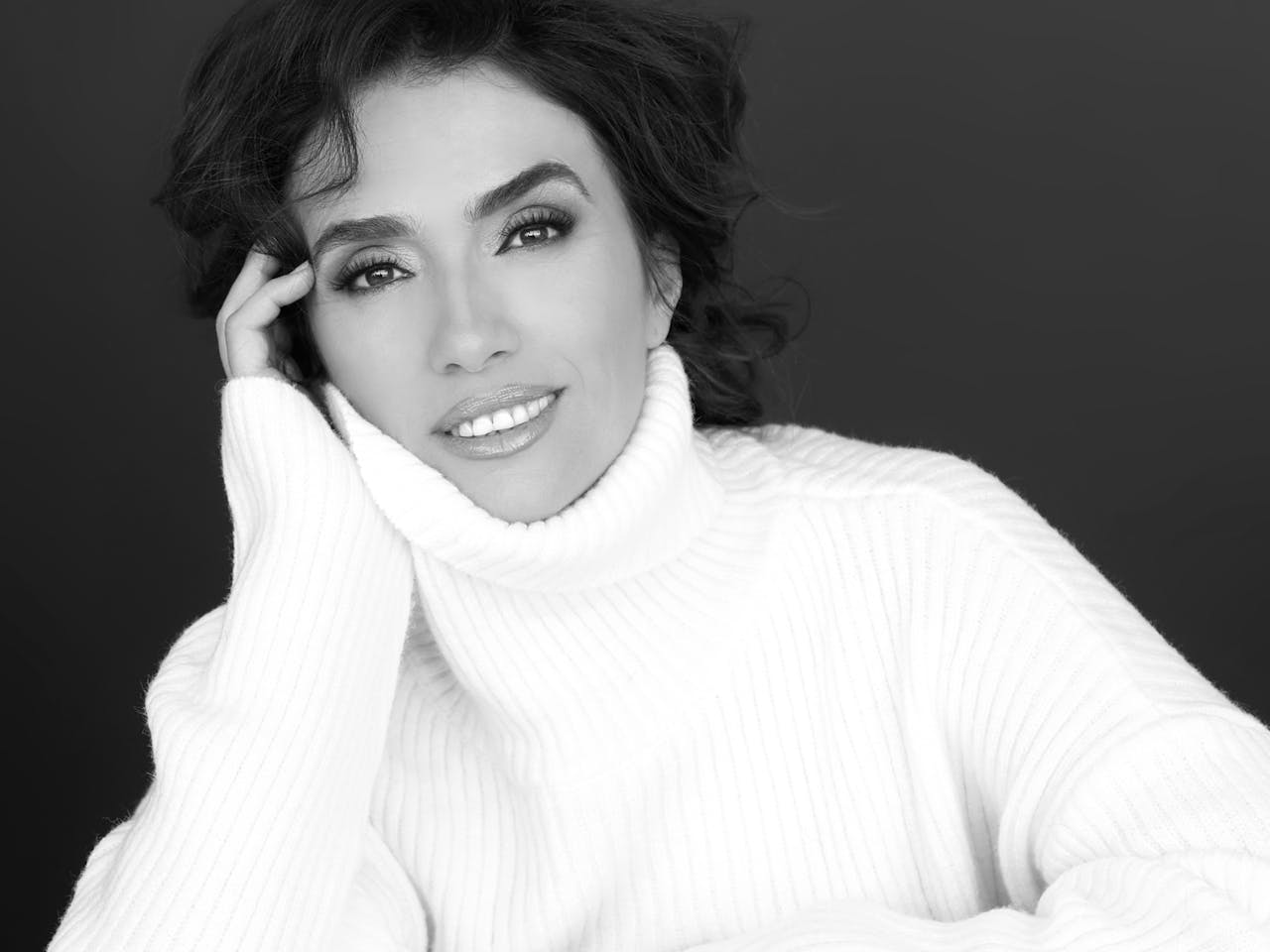 Headshot in black and white of the opera singer Ermonela Jaho wearing a white rollneck jumper.