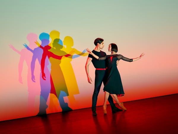 two dancers embrace under a light. Their shadows are behind them and are coloured pink green and yellow
